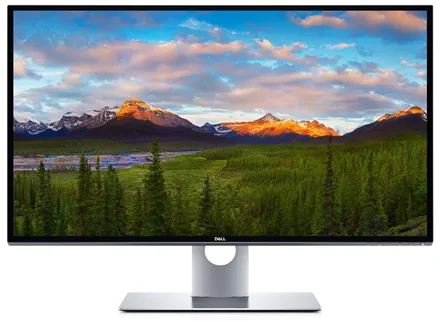 Монитор Dell UltraSharp 8K UP3218K с широким экраном, на котором изображён захватывающий пейзаж: заснеженные горные вершины, освещённые закатным солнцем, густой хвойный лес на переднем плане и яркое небо с облаками