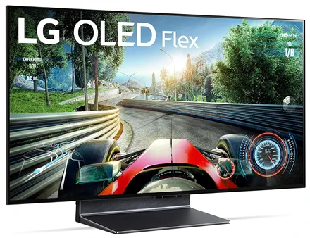 На изображении представлен телевизор LG OLED Flex 42 — инновационная модель с управляемой кривизной экрана. На экране демонстрируется яркая игровая сцена: вид из кабины гоночного болида на извилистой трассе, окружённой зелёными деревьями и горами. В верхней части экрана крупно размещён логотип «LG OLED Flex»