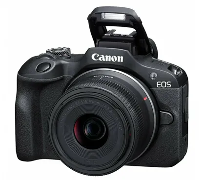 На изображении представлена беззеркальная камера Canon EOS в чёрном корпусе. Вспышка поднята, демонстрируя готовность к съёмке. На переднем плане виден установленный объектив. Логотип «Canon» отчётливо заметен в верхней части корпуса, справа обозначена серия «EOS»
