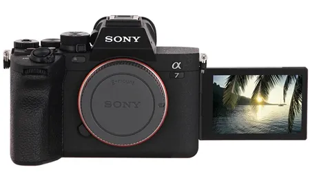 На изображении представлена беззеркальная камера Sony Alpha 7 IV (ILCE-7M4) в чёрном корпусе. Откидной экран развёрнут, на нём отображается фотография с видом на закат над водой и пальмами. Видны основные элементы камеры: байонет с красной окантовкой, логотип «SONY» и маркировка модели «α7 IV»